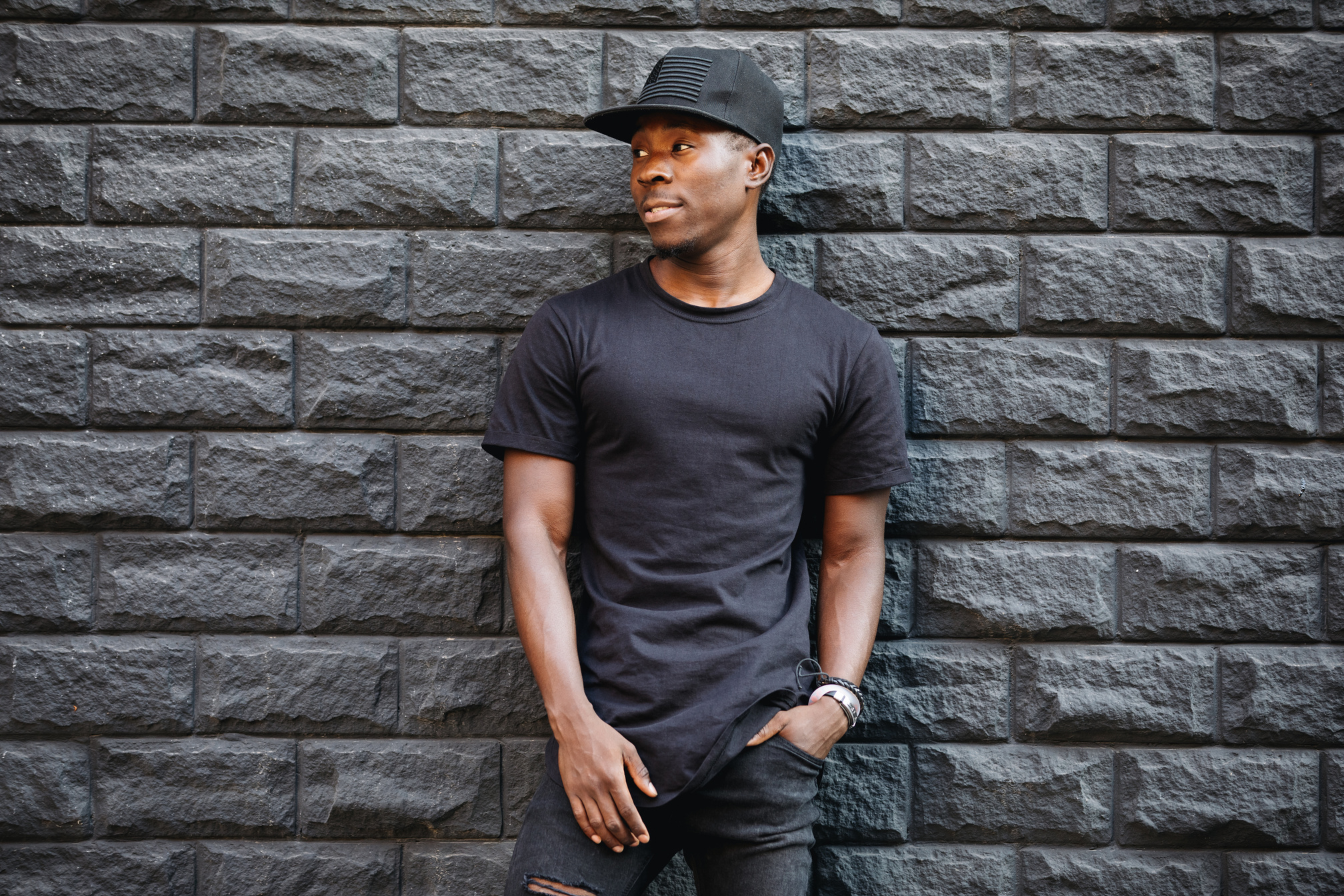 Handsome african american man in blank black t-shirt standing against brick wall